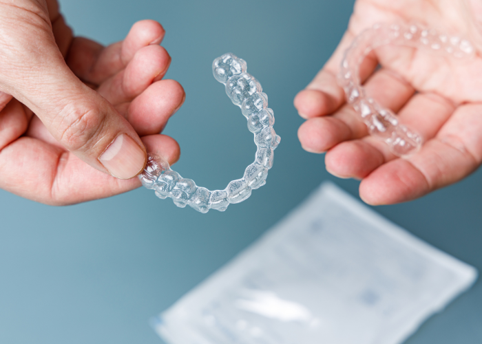 A pair of hands holding a set of clear aligners used to straighten teeth over time.